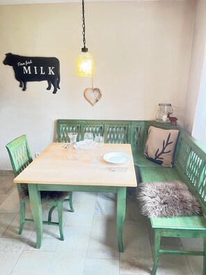 A dining area with a wooden table, green chairs, a bench, and a wall decoration of a cow and heart.