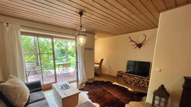 Una sala de estar con techo de madera, televisor, sofá, mesa de centro y alfombra de cuero de vaca.