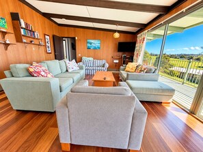 A modern living room with a large window, a flat-screen TV, and a wooden ceiling. - Sylvin Waters, Mallacoota (Mallacoota)