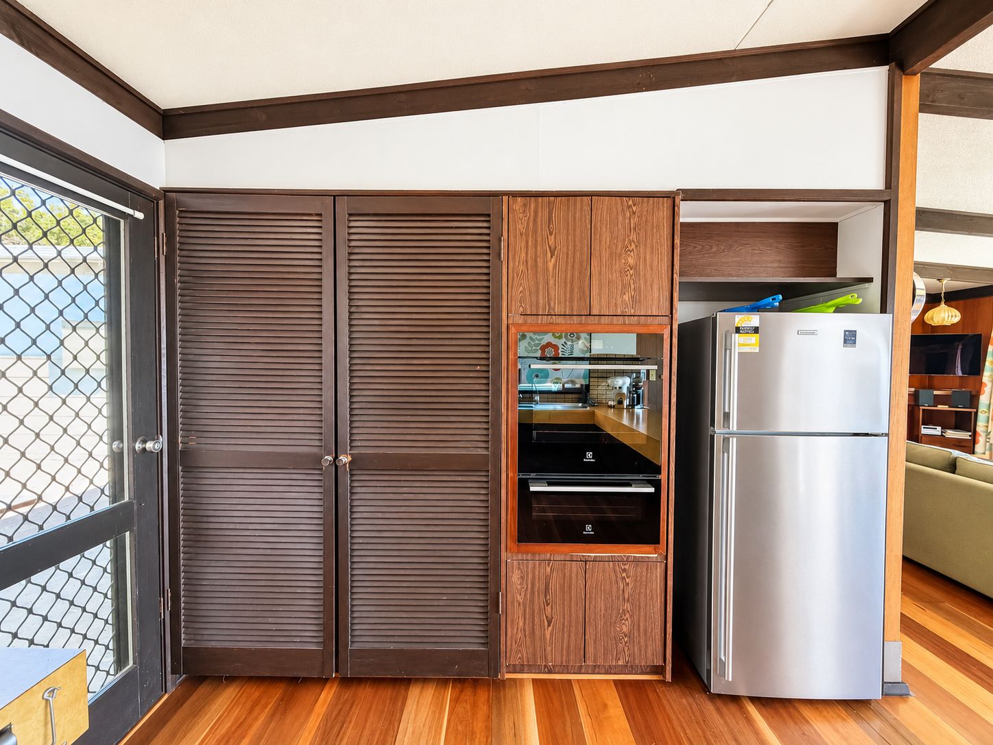 Eine kompakte Küche mit Backofen, Edelstahlkühlschrank und Holzschränken.