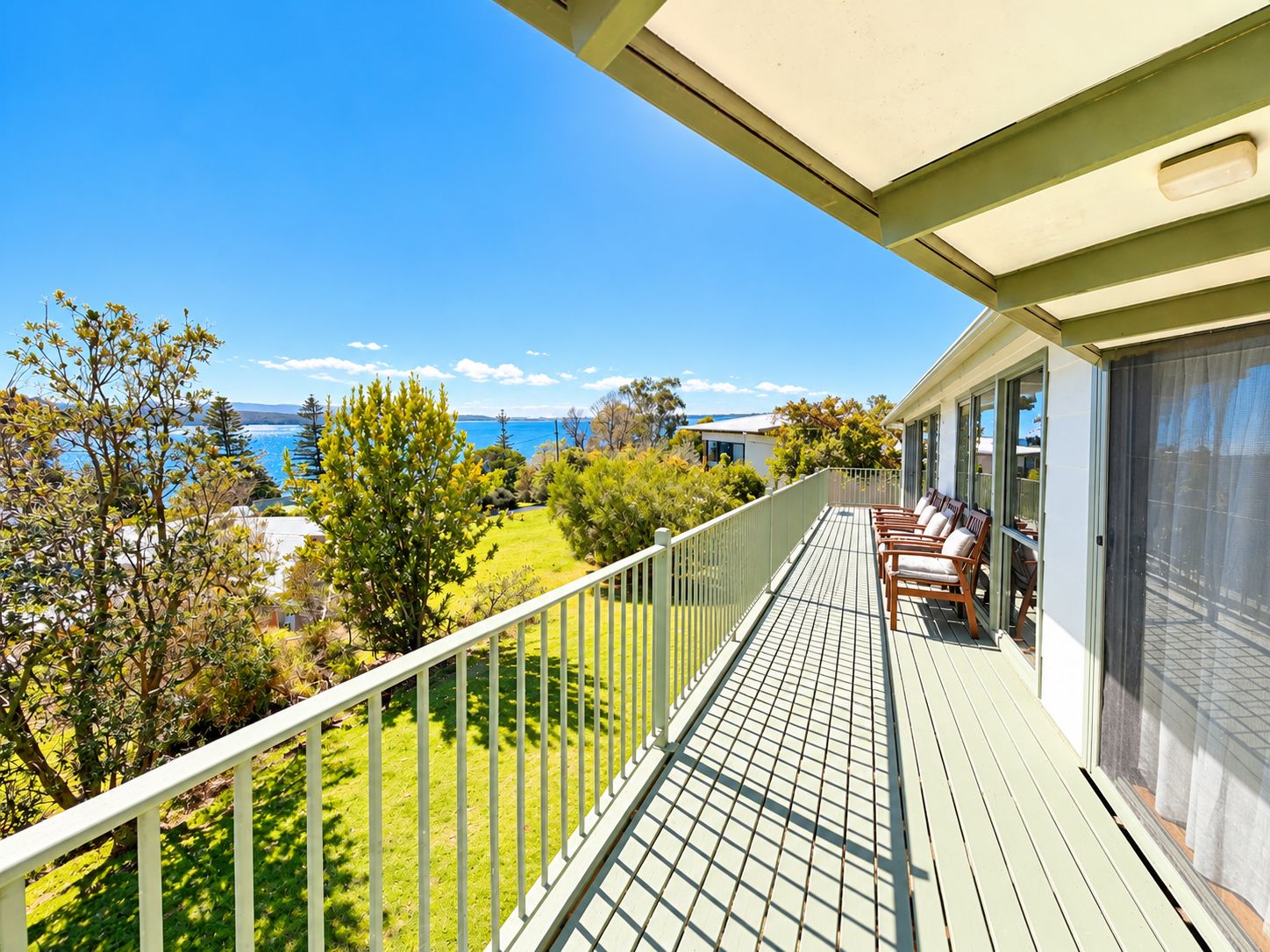 Un balcon avec vue sur la mer, une pelouse et une rangée de chaises.