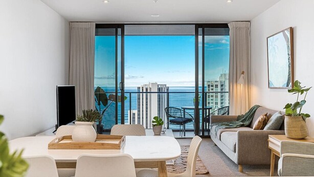 A modern living room with a large sliding glass door leading to a balcony with a city view.