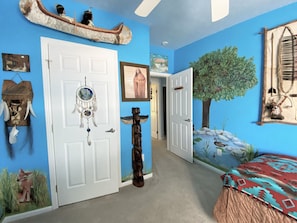 A room with a blue wall, a white door, a dreamcatcher, a totem, and a mural of a tree and ducks.