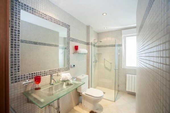 Un baño moderno con cabina de ducha de vidrio, lavamanos de vidrio y un inodoro blanco.