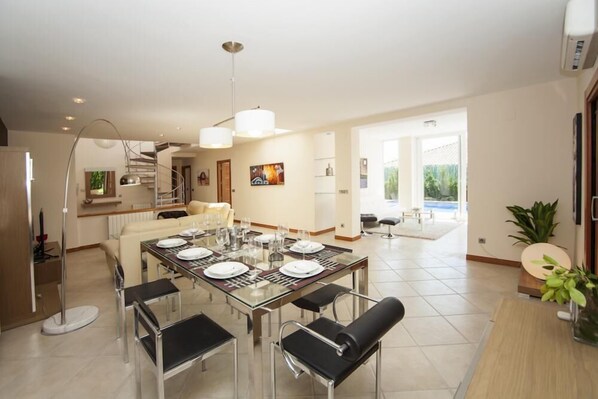 A modern dining area with a glass table, black chairs, and a chandelier.