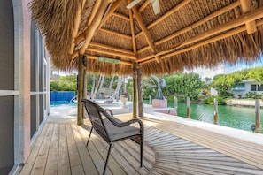 Eine Holzterrasse mit einem Reetdach, mit Blick auf einen Pool und ein Wasserspeicher.