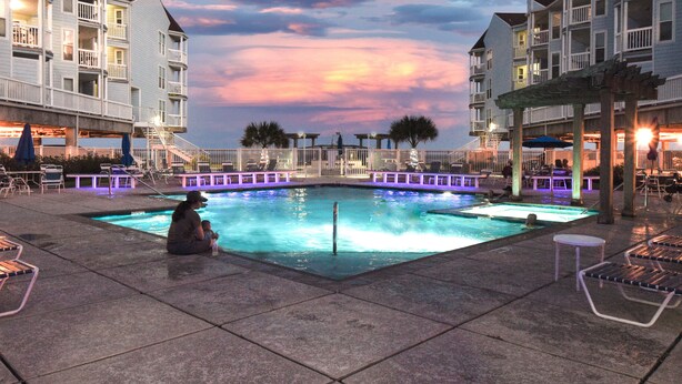 A pool area with a woman and child, surrounded by buildings with balconies and outdoor seating.