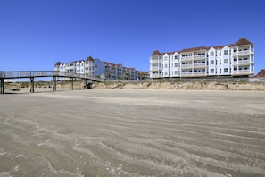 A beachfront hotel with multiple balconies, a wooden boardwalk, and a sandy beach.