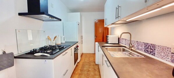 Una cocina compacta con estufa a gas, armarios blancos, microondas y lavamanos.