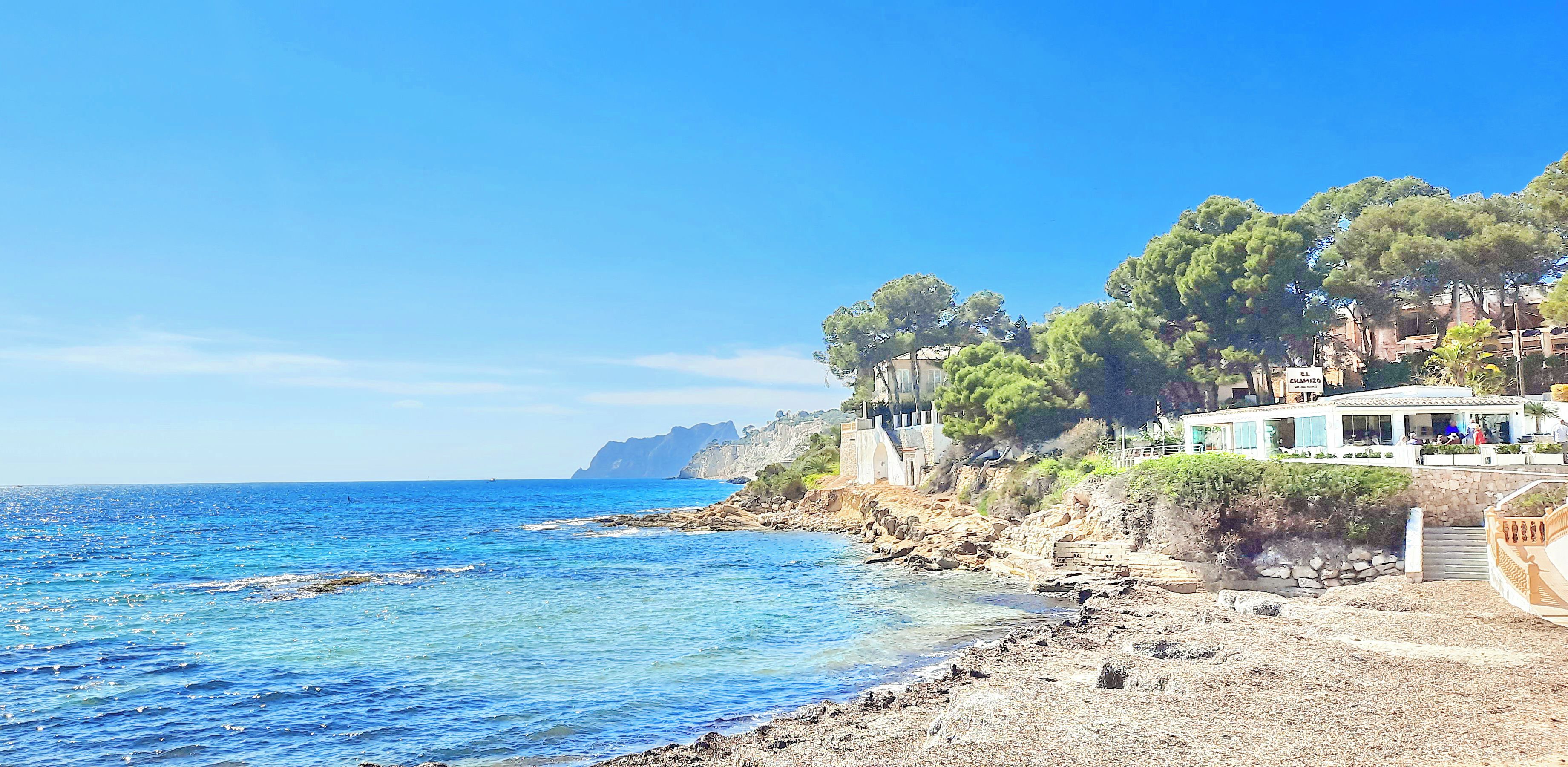 A coastal hotel with a rocky shoreline, clear blue sea, and lush greenery.