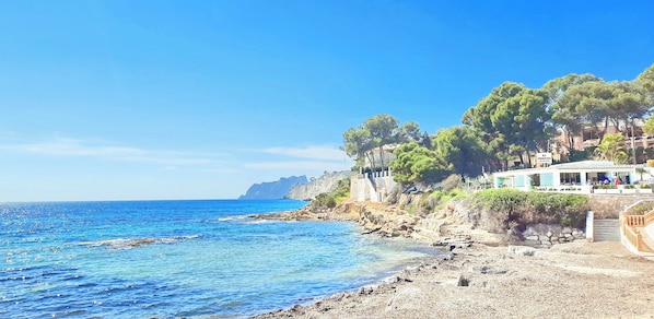 A coastal hotel with a rocky shoreline, clear blue sea, and lush greenery.