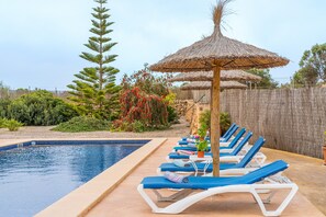 Una piscina con sillones de descanso y una sombrilla de paja.