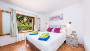 Quarto com cama, janela com cortinas, radiador, mesa de cabeceira com planta e uma obra de arte na parede.