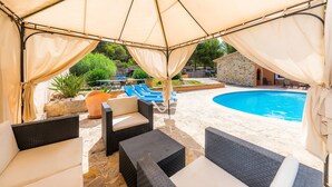 Espaço coberto ao ar livre com espreguiçadeiras e piscina.