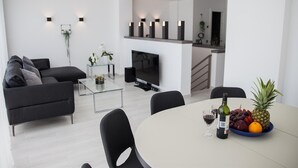 A modern living room with a sofa, coffee table, TV, and a dining area with a table set for two. - Spacious Sea View Penthouse with Sea View, Wi-Fi & Terrace (Torremolinos)