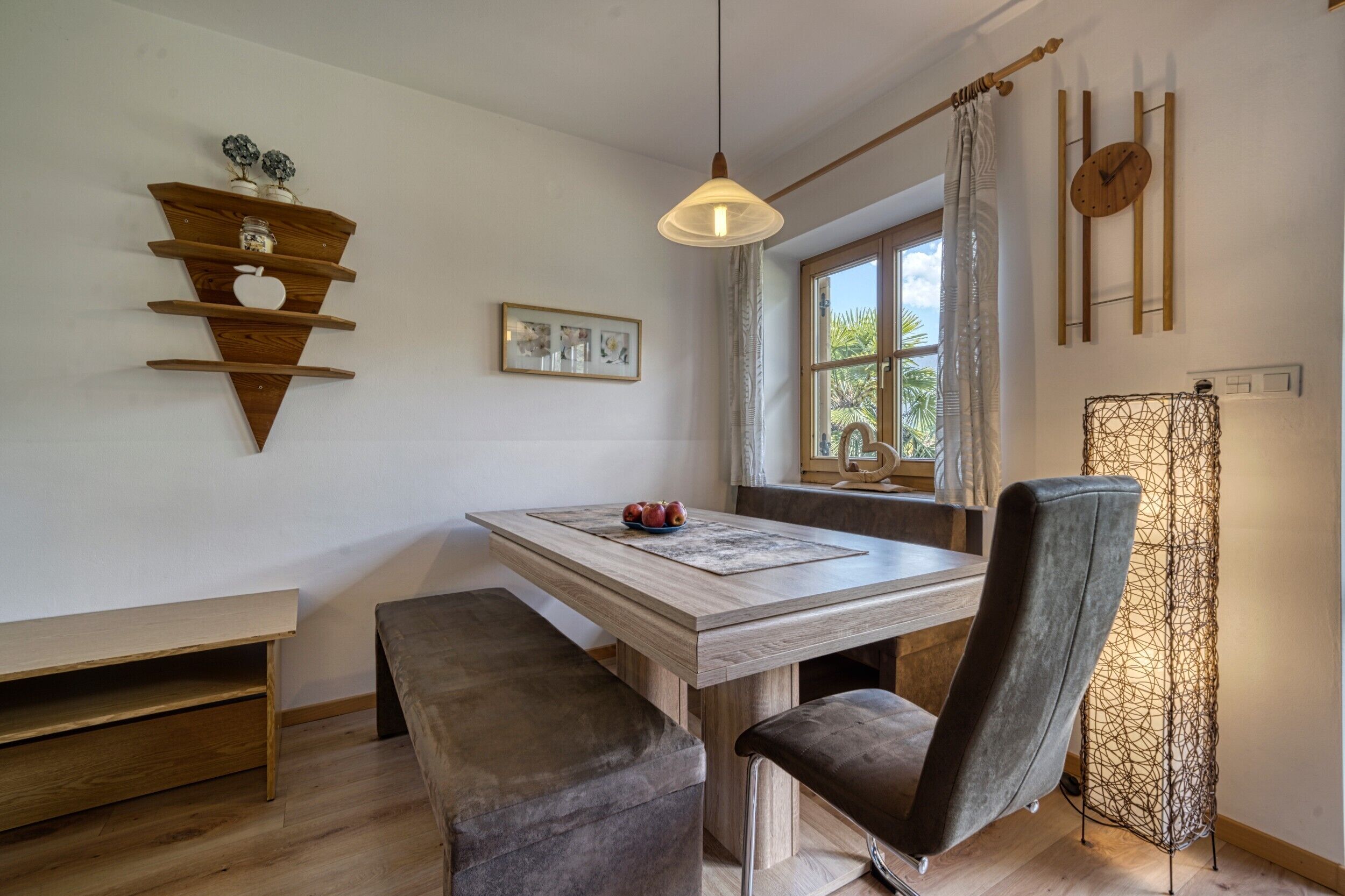 Uma área de refeições com mesa de madeira, bancos, luminária pendente e vista para o exterior.