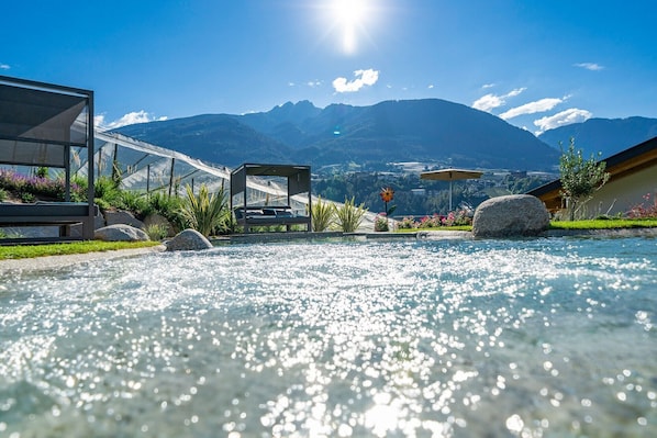 Une piscine avec vue sur les montagnes, un fauteuil de relaxation et un bâtiment moderne.