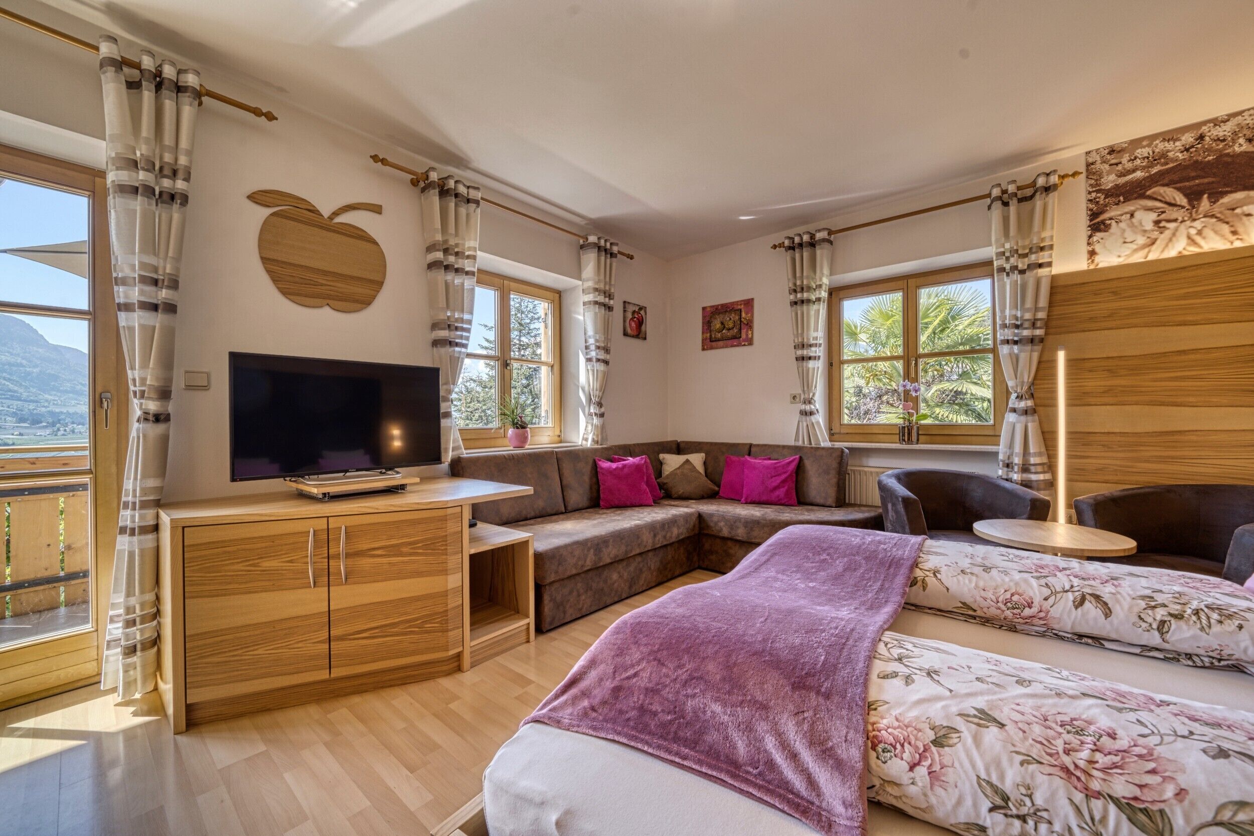 A modern living room with a TV, sofa, and a bed with floral bedding.