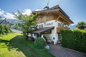 A two-story building with a sign 'Feldhof Apartments Chalet' and a view of a mountainous landscape. - Apartment "Feldhof Apfeltraum" with Saltwater Pool, Panoramic Lawn and Balcony (Kuens bei Meran)