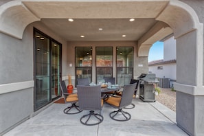 An outdoor patio with a round table and chairs, a grill, and a view of the surrounding area.