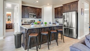 A modern kitchen with dark wooden cabinets, stainless steel appliances, and a central island with bar stools. - Paseos 1121, Sleeps 15, Private Pool, Hot Tub (Washington)