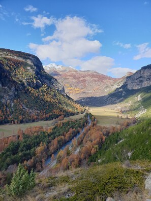A mountainous landscape with a valley, a river, and a distant snow-capped peak.