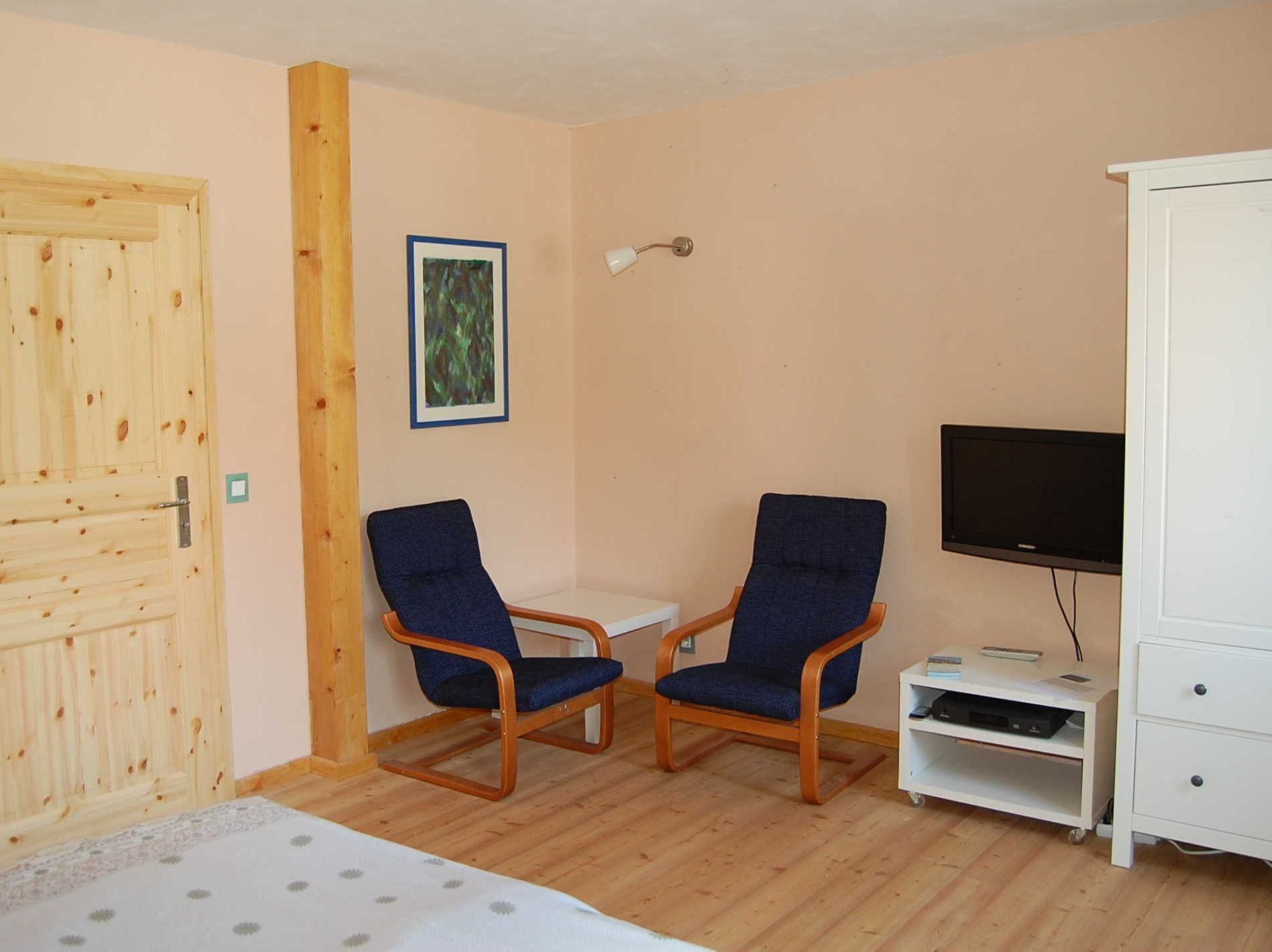 A room with two blue chairs, a small table, a TV on a stand, a white cabinet, and a wooden door.