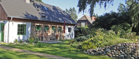 A two-story house with a sloped roof, a stone wall, and a garden with a paved path.