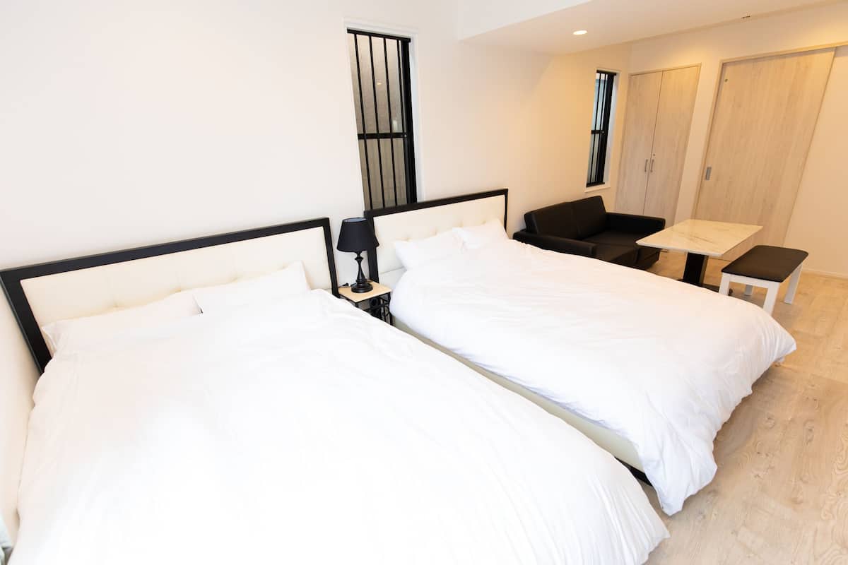 Ein Hotelzimmer mit zwei Einzelbetten, einem kleinen Tisch, einem Stuhl, einem Schrank und einem Fenster mit Gitterstäben.