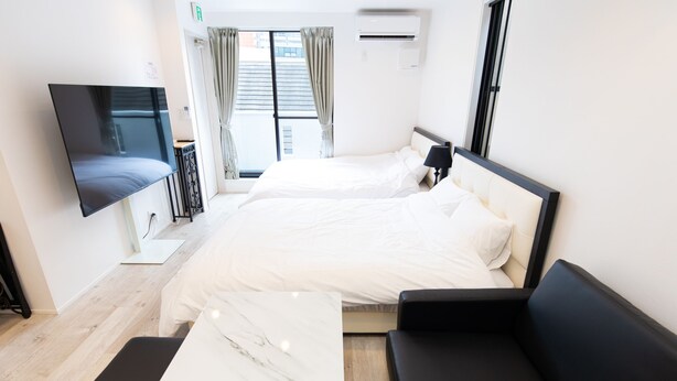 Una habitación de hotel moderna con una cama grande, un televisor de pantalla plana, un sofá negro y una pared de acento de mármol.