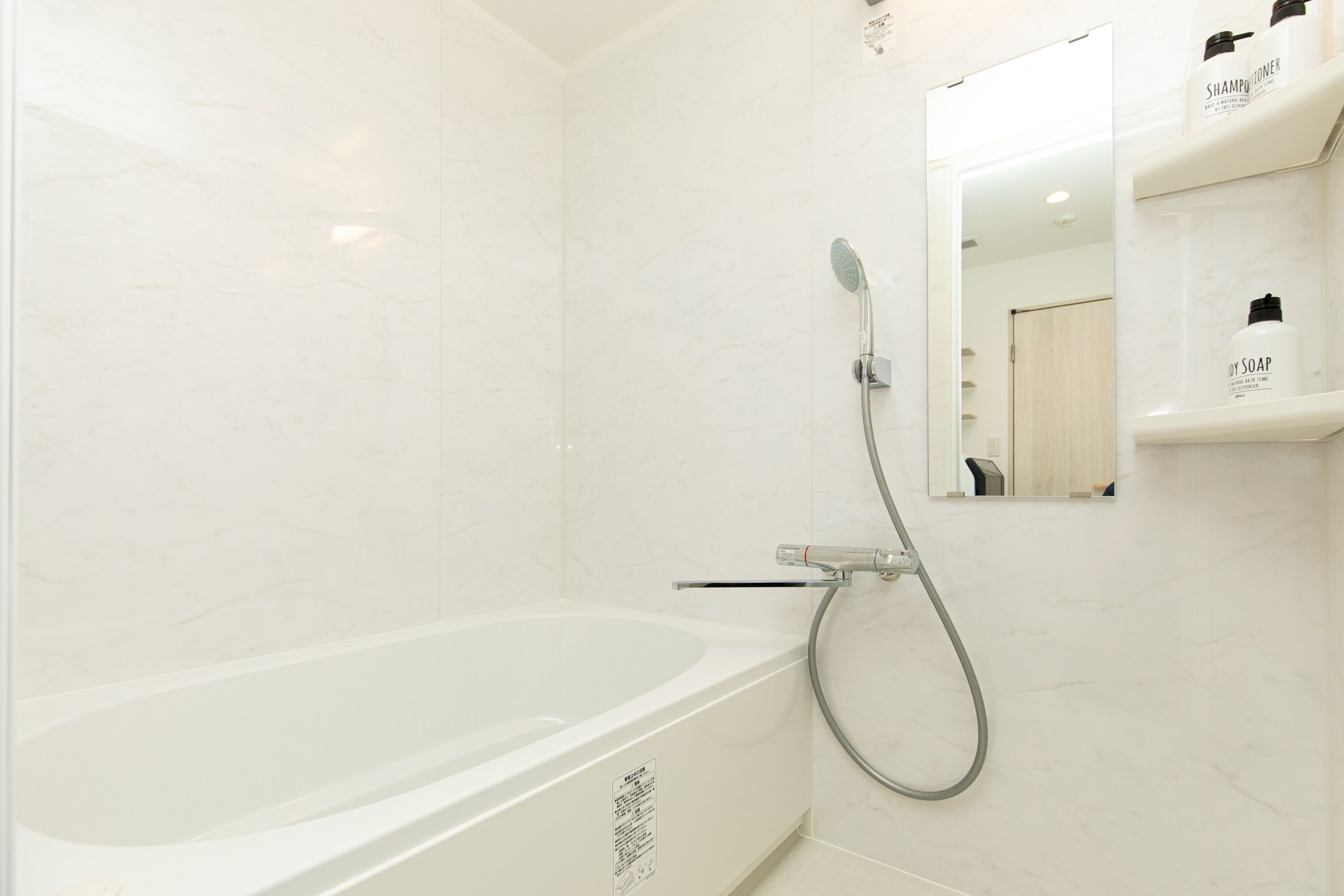A modern bathroom with a white bathtub, a handheld showerhead, and a mirror above a shelf with toiletries.