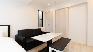 Un dormitorio moderno con un sofá negro, una cama blanca, una mesita de mármol y un armario de madera.