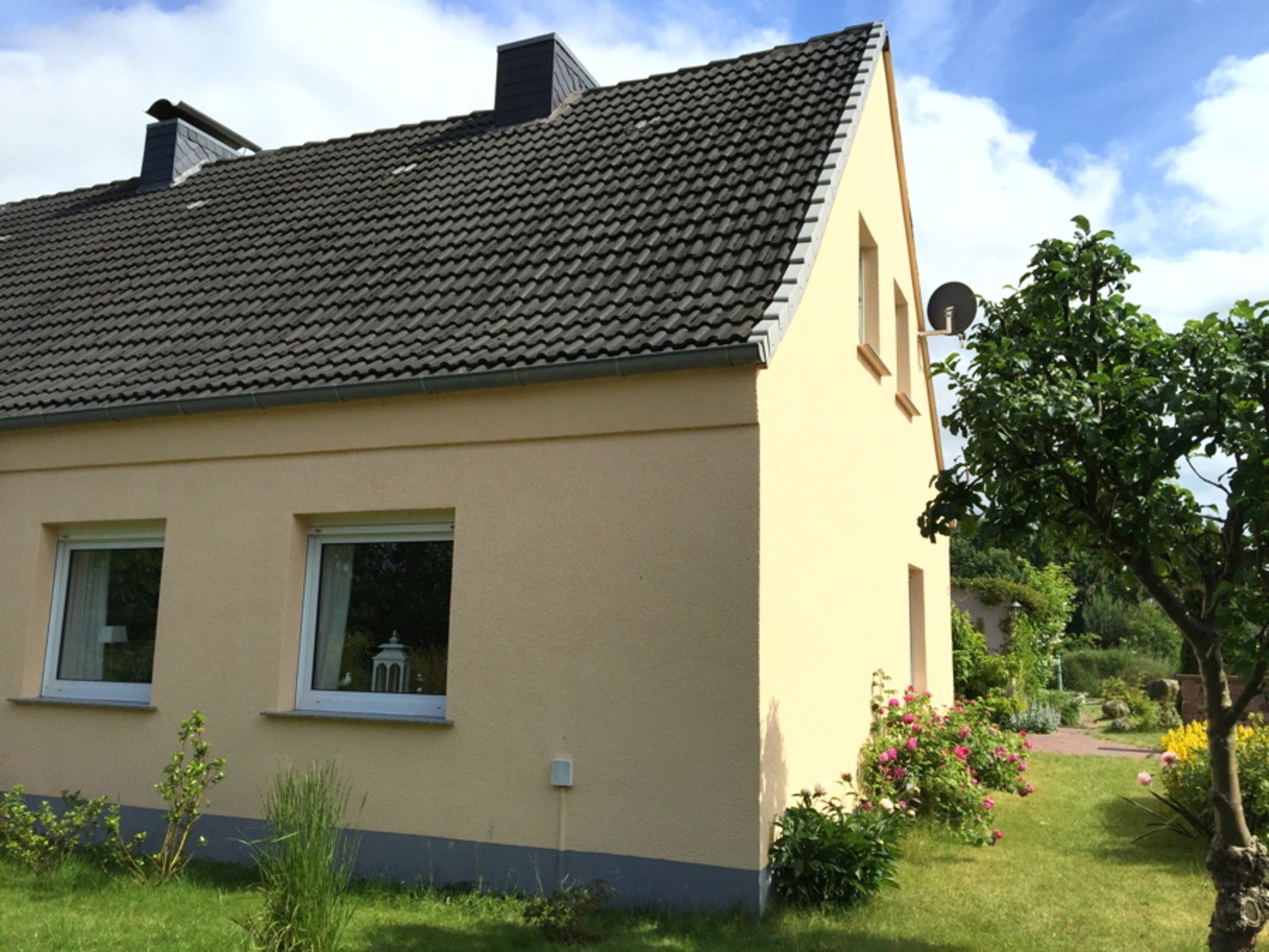 Et toetagers hus med tegltag, en lille have med blomster og en parabol på siden.