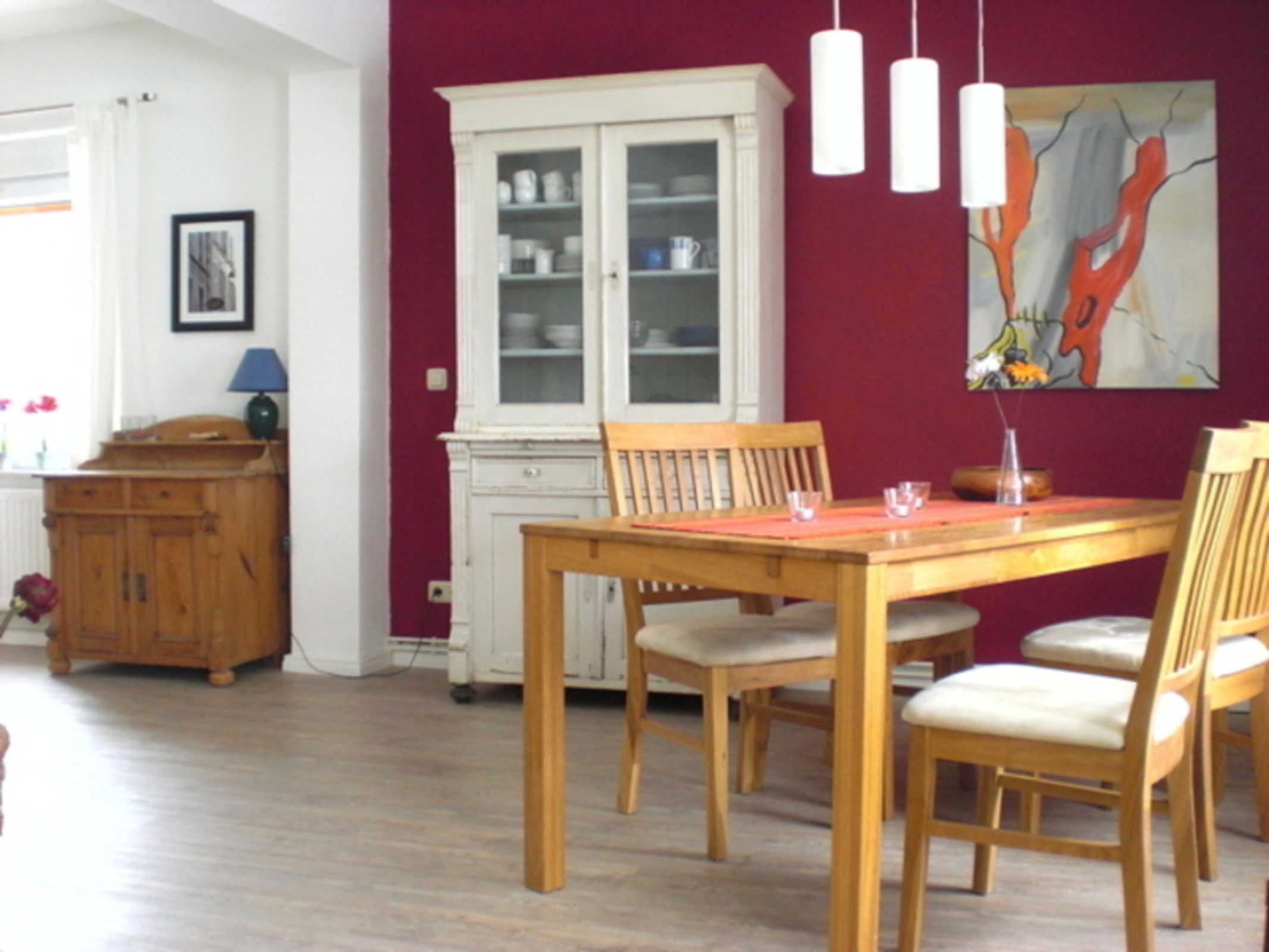 A dining area with a wooden table and chairs, a white cabinet, and a painting on the wall.
