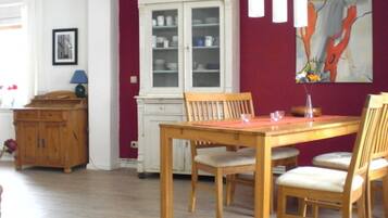 A dining area with a wooden table and chairs, a white cabinet, and a painting on the wall.
