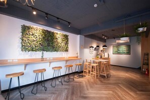 A modern bar area with wooden stools, a long counter, and a green leafy wall decoration. - Luke 27 (Tainan)