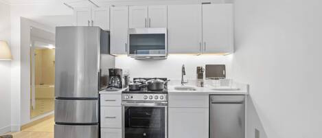 A compact kitchen with white cabinets, stainless steel appliances, and a built-in oven.