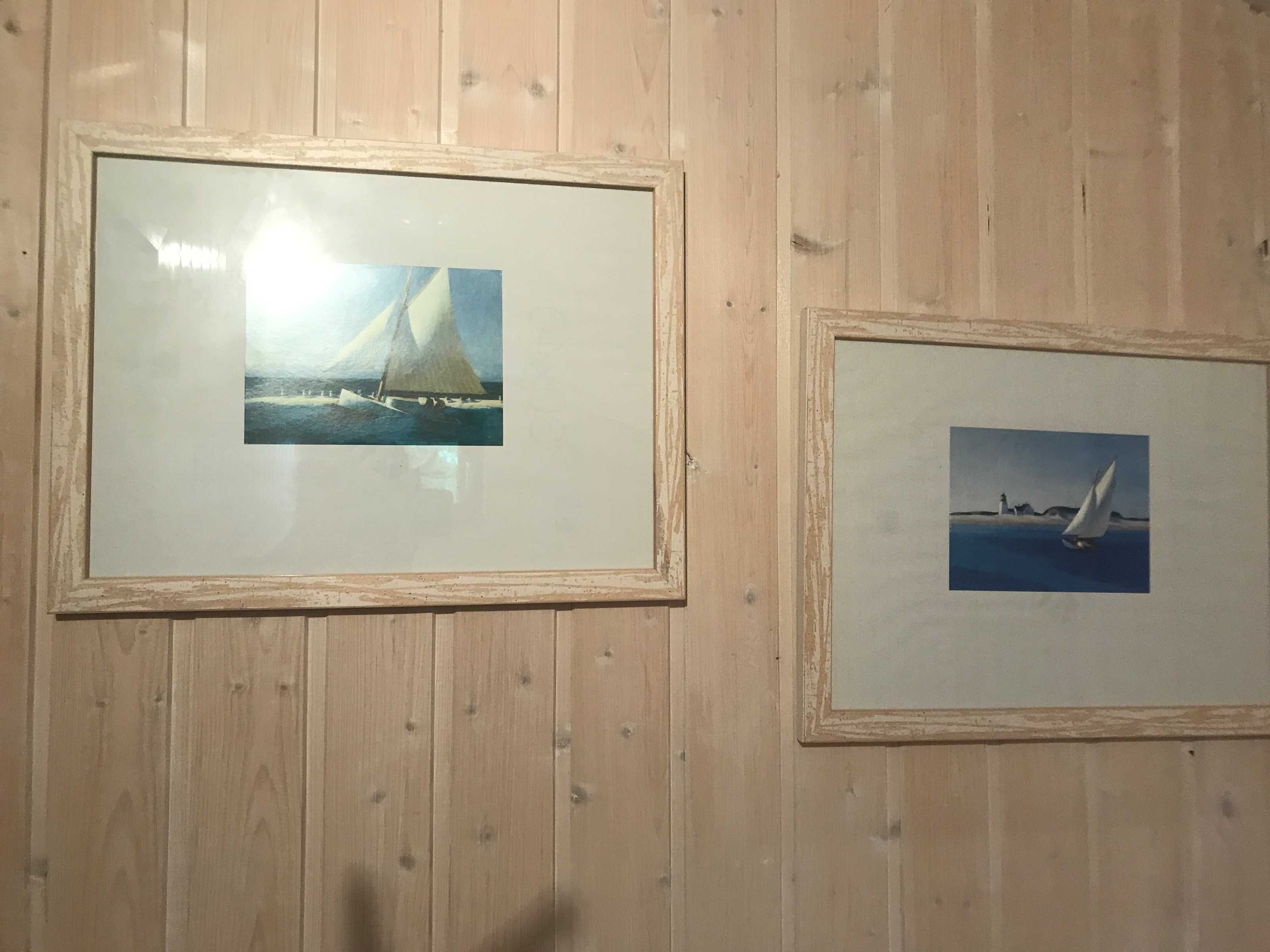 Two framed pictures of sailboats on a wooden wall.