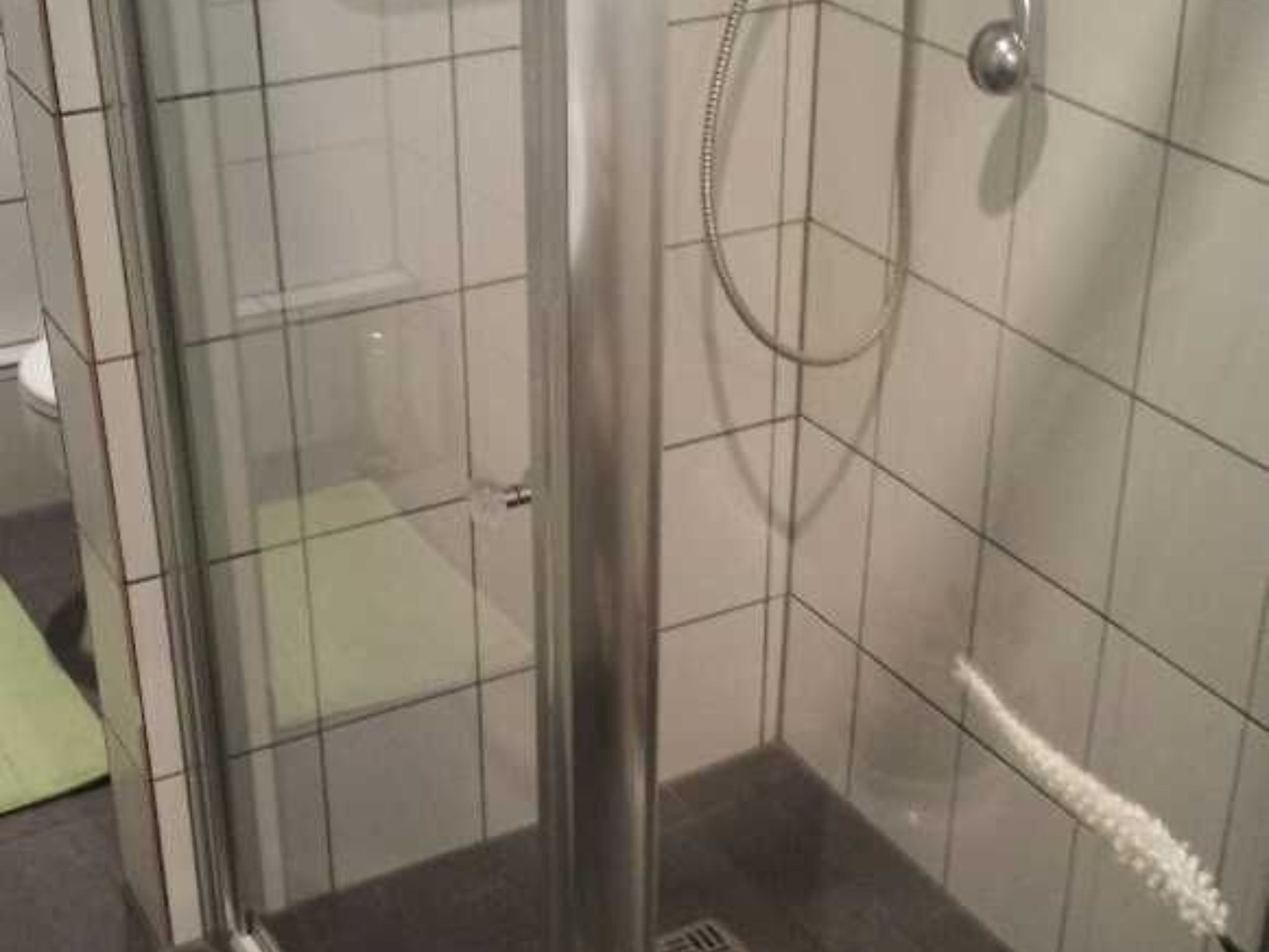 A glass-enclosed shower stall with a handheld showerhead and a wall-mounted faucet.