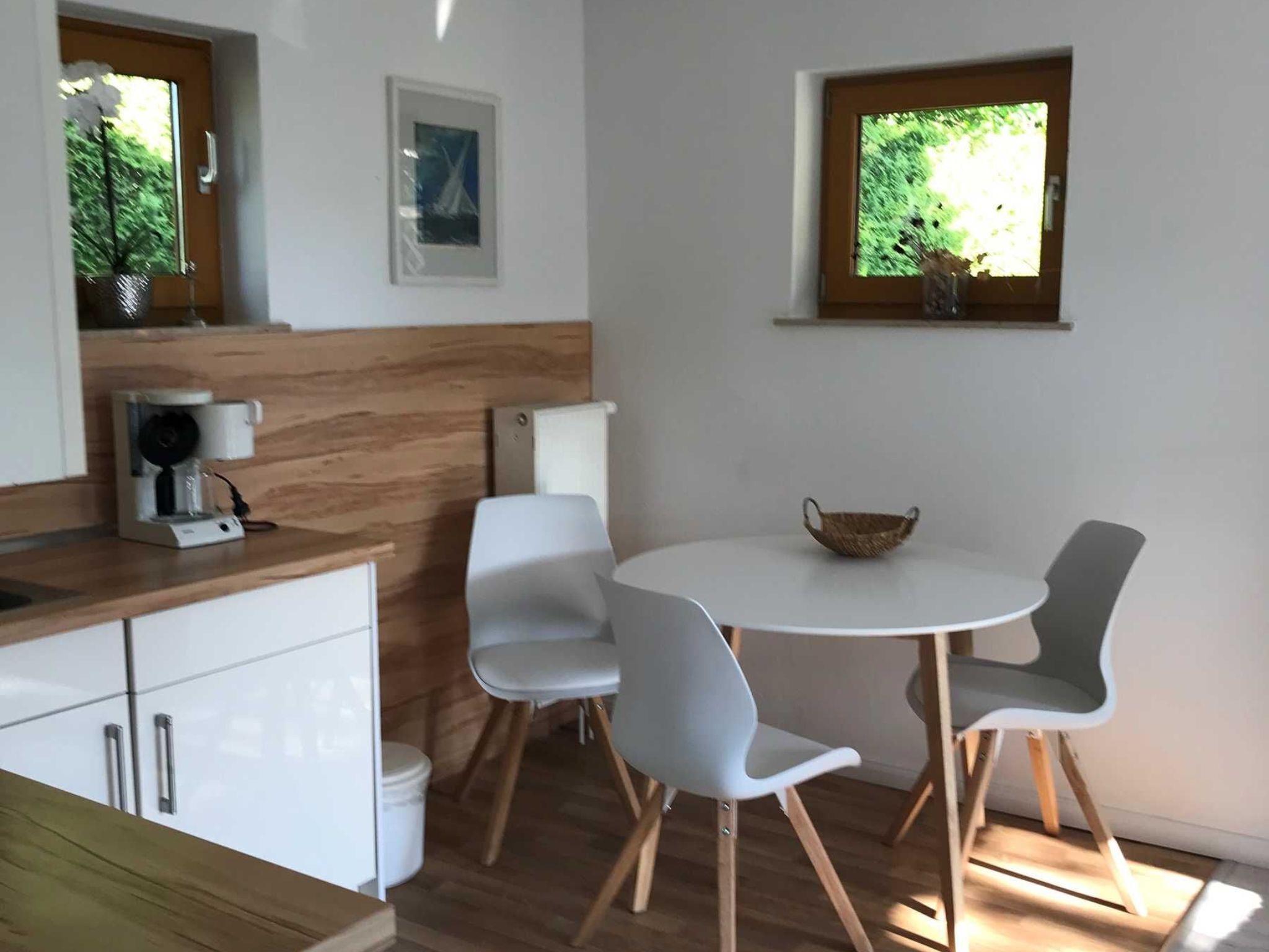 Une cuisine moderne avec des meubles blancs, une machine à café et une table de salle à manger ronde, accompagnée de quatre chaises.