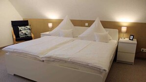 Quarto de hotel com uma cama grande, duas mesas de cabeceira, uma cadeira e uma luminária na parede.