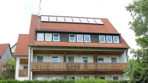 Edifício residencial de vários andares com telhado de telhas vermelhas, varandas de madeira e painéis solares.