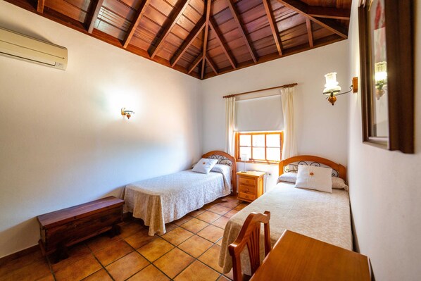 A bedroom with two beds, a wooden bench, a small table, and a window with curtains. - El Manso, Tijarafe, Spain (Tijarafe)