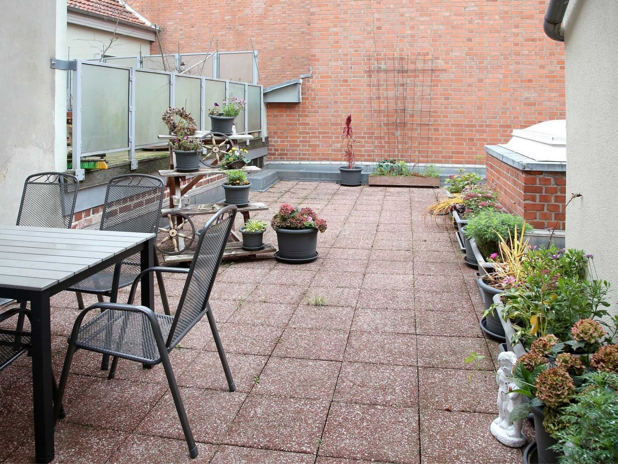 Eine Terrasse mit Tisch und Stühlen, umgeben von Topfpflanzen und einer Backsteinmauer.