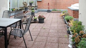 Une terrasse avec une table et des chaises, entourée de plantes en pot et d’un mur en briques.