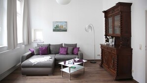 Un salon moderne avec un canapé gris, une table basse en verre, un meuble en bois et un tableau accroché au mur.