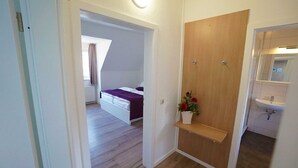 Une chambre à coucher avec un lit, une porte en bois, une petite étagère avec des fleurs et une salle de bain avec un lavabo et un miroir.