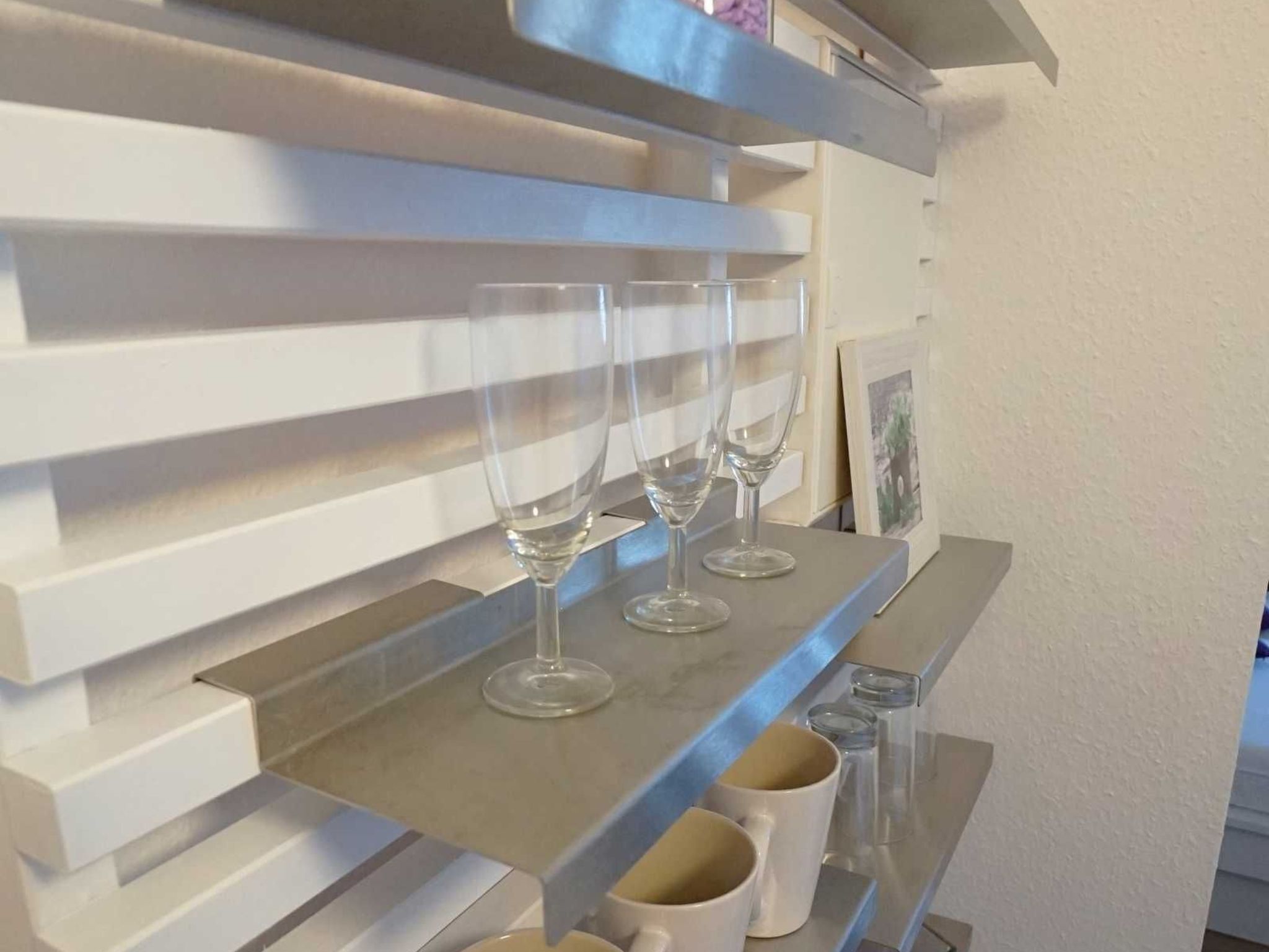 Una cocina moderna con una estantería para vinos que contiene tres copas y un estante con dos tazas blancas.