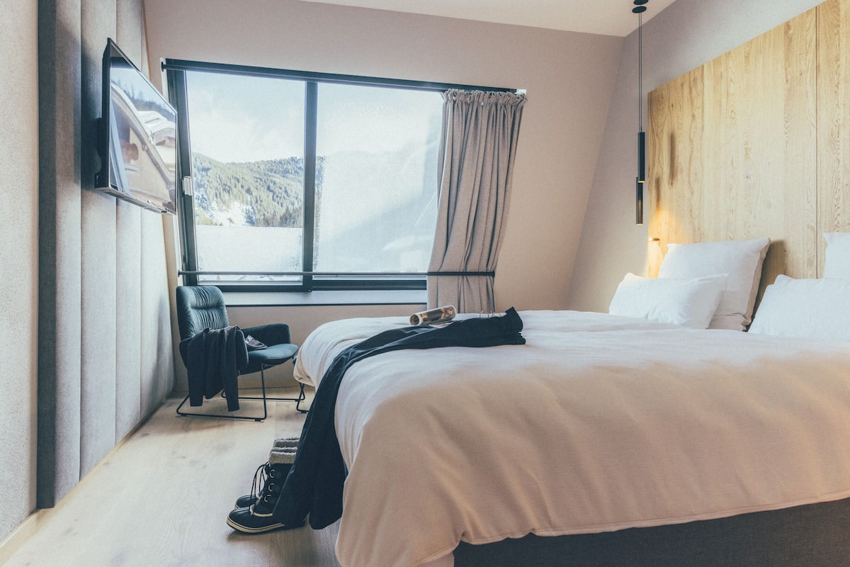 Une chambre d’hôtel avec un grand lit, une chaise, un bureau et une fenêtre donnant sur les montagnes.