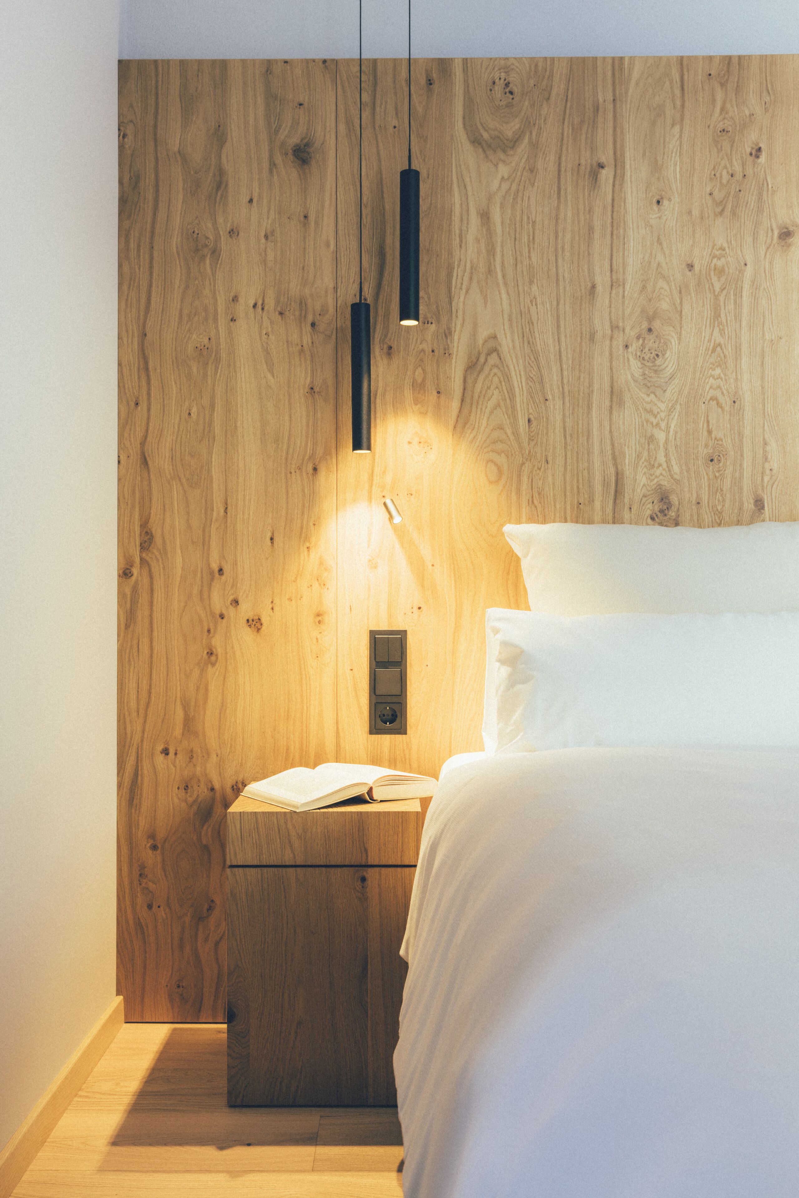 A bedroom with a wooden headboard, a bedside table with a lamp, and a bed with white bedding.